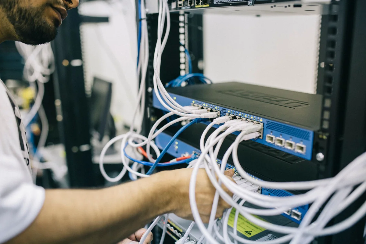 Technician connecting white network cables to a switch in a server rack
